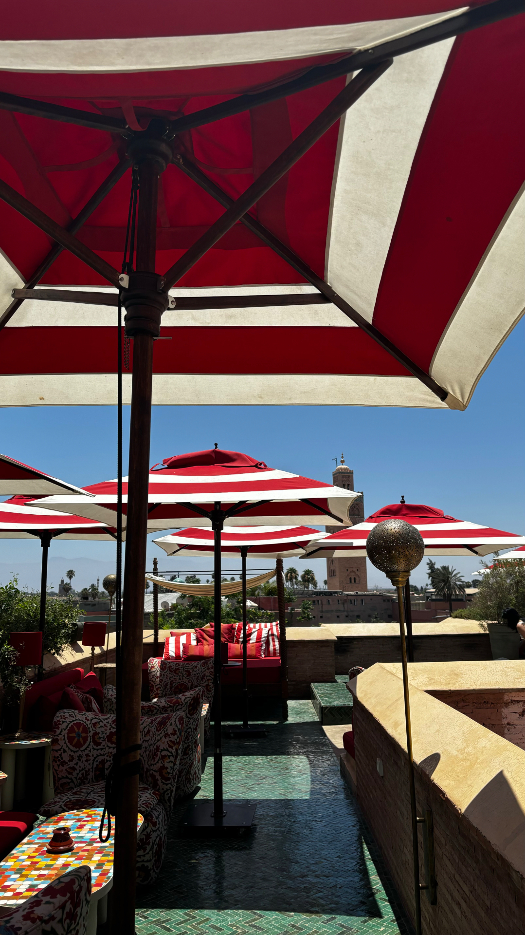 Terrasse du rooftop El Fenn à Marrakech avec parasols rouges et blancs et vue sur la Koutoubia