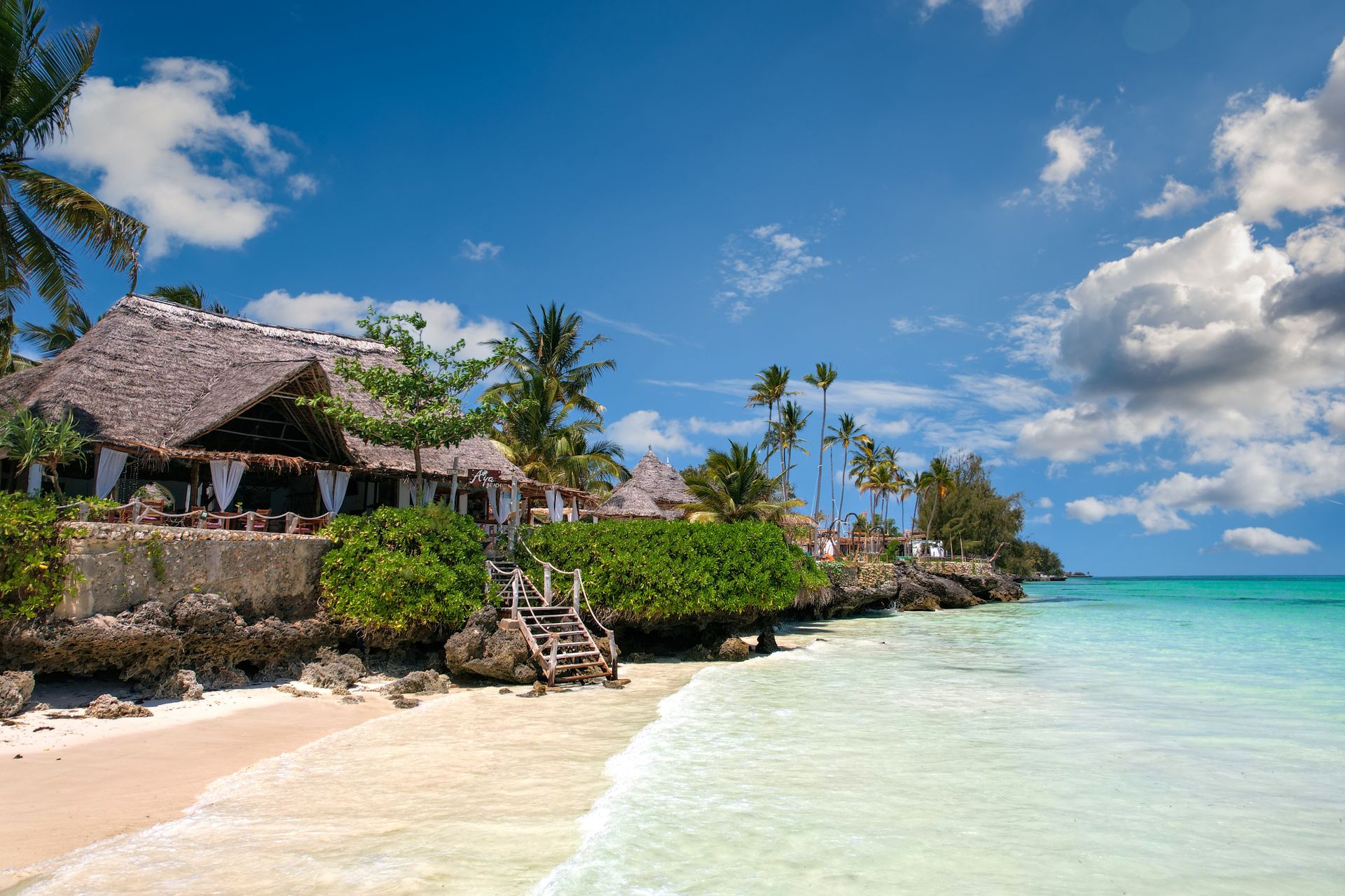 Plage de Zanzibar, eau turquoise cristalline, toit de chaume et palmiers