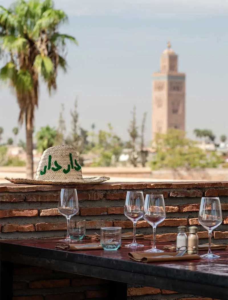 Table dressée sur le rooftop DarDar à Marrakech avec chapeau de paille et vue sur la Koutoubia