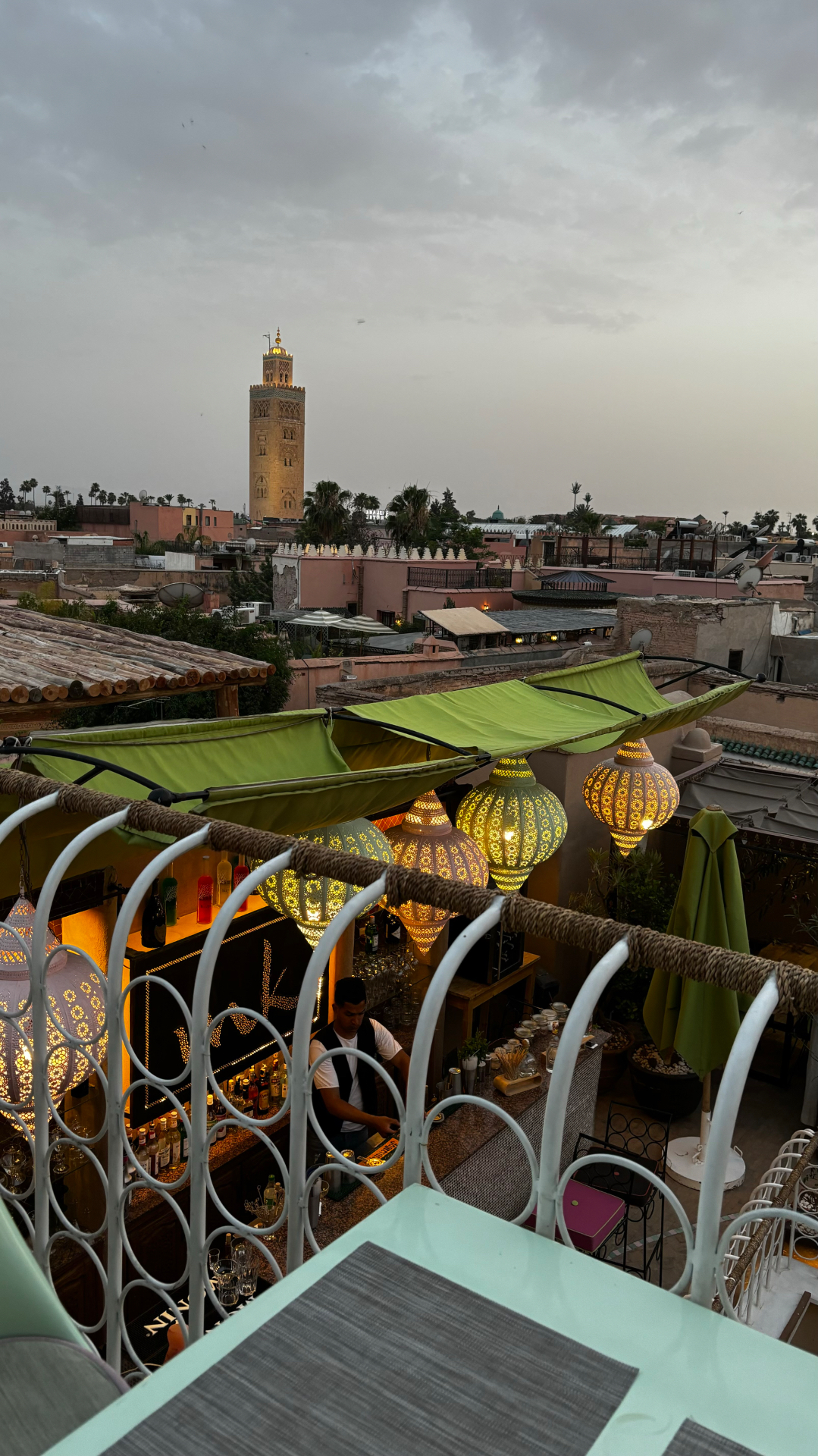 Terrasse du MK Rooftop à Marrakech au crépuscule avec lanternes, tonnelles vertes et vue sur la Koutoubia